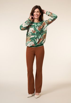 Langermige top in groen, bruin en crèmekleurig bloemenpatroon; gecombineerd met bruine flared broek en crèmekleurige spitse hakken. Glad stoffen textuur.
