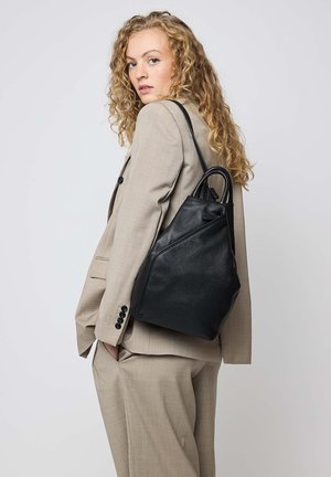 Black leather bag with a triangular shape, featuring a smooth texture, dual handles, and a subtle seam detail. Worn over a gray suit.