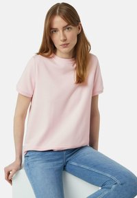 Lichtroze T-shirt met korte mouwen en een ronde hals; gemaakt van zacht katoen met een relaxed fit, gecombineerd met lichtblauwe jeans. Eenvoudig ontwerp.