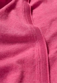 Růžová pletenina s hladkým povrchem, viditelným švem a žebrovanými akcenty. Materiál vypadá lehce a jemně.