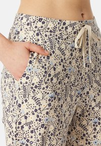 Pantalon en coton avec une base crème et un motif floral en bleu, marine et jaune. Comprend des poches latérales et une taille à cordon.