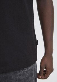 Svart bomull T-skjorte med rett snitt, med en liten stofflapp på siden. Stoffet ser mykt og glatt ut i teksturen.