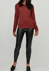 Pull rouge à manches longues avec un col rond, associé à des leggings en faux cuir noir moulants. Texture lisse et design ajusté.