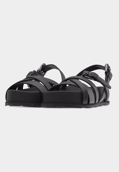 Μαύρα πλατφόρμα σανδάλια με τρεις μπροστινές λωρίδες, λουριά αστραγάλου με ρυθμιζόμενες ασημένιες αγκράφες και επίπεδες λαστιχένιες σόλες σε λευκό φόντο.