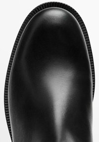 Bottine noire à talon avec un matériau synthétique lisse, un bout arrondi et des bords côtelés. Présente une finition brillante et un design de dessus renforcé.