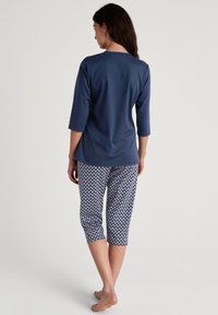 Donkerblauw driekwartmouwtop met een ronde hals, gecombineerd met geprinte cropped broek met een geometrisch patroon in wit en blauw.