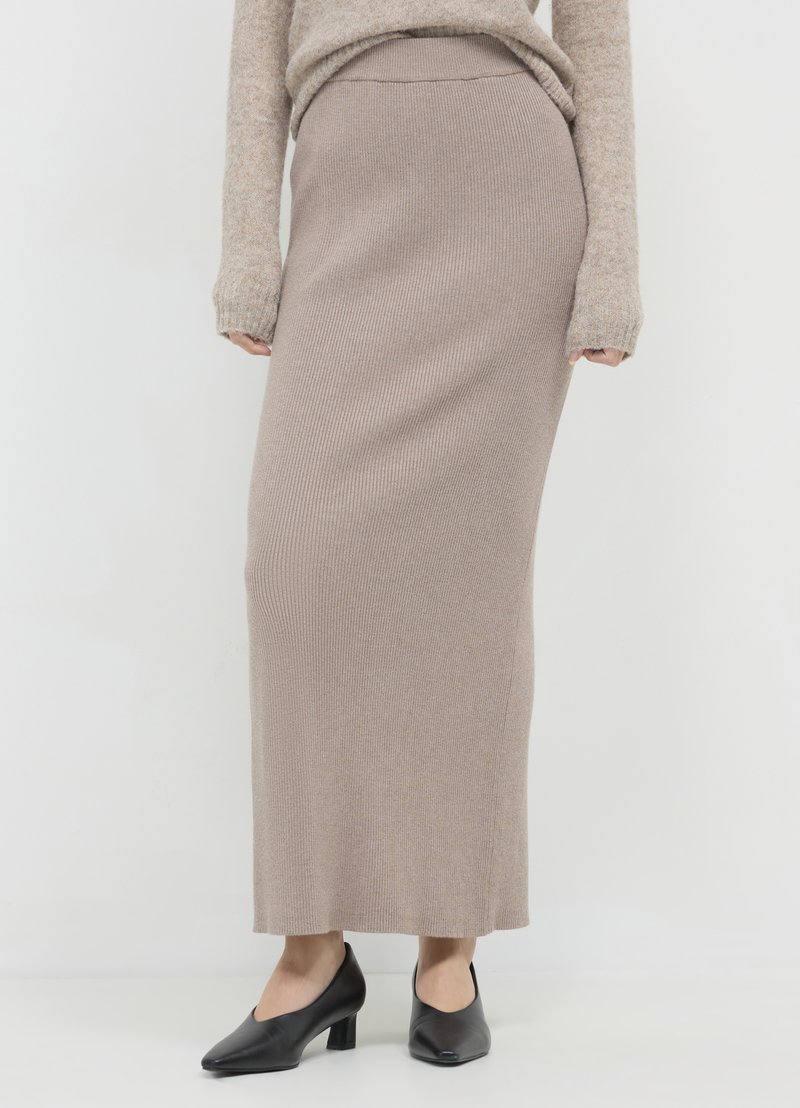 Jupe longue en maille côtelée beige clair, associée à des chaussures à talons noires. Le matériau a une texture douce et une silhouette ajustée.