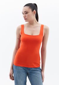 Top de tirantes ajustado naranja con escote cuadrado y tirantes anchos, fabricado en una tela lisa y elástica. Llevado con jeans de cintura alta.