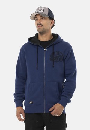 Haut de survêtement zippé bleu marine avec poches kangourou et capuche à cordon ; présente un imprimé de logo noir et des accents gris à l'intérieur et sur le chapeau.