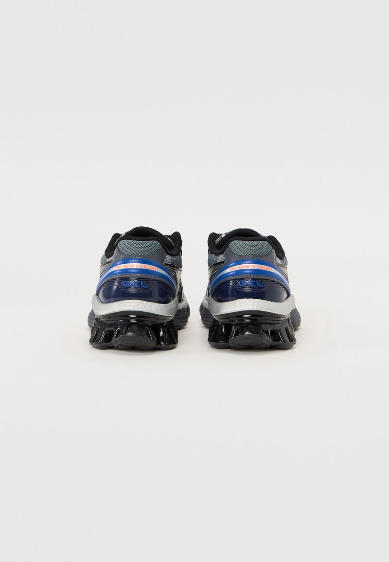 Zapatillas de correr negras y grises con parte superior de malla texturizada, acentos reflectantes y una suela estriada distintiva para amortiguación.