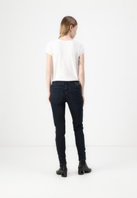 Jeans skinny azul oscuro con bolsillos traseros, combinados con una camiseta blanca de manga corta. Estilizados con botas negras de tobillo.