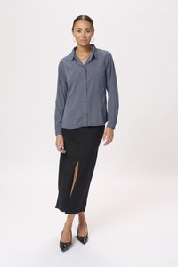 Chemise à manches longues grise à boutons associée à une jupe noire ajustée longueur cheville avec une fente à l'avant, et des escarpins noirs à bout pointu.