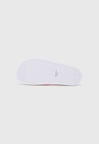 Semelle de chaussure en caoutchouc blanc avec un motif en losanges texturé, dotée d'une petite étiquette et d'un bord arrondi.