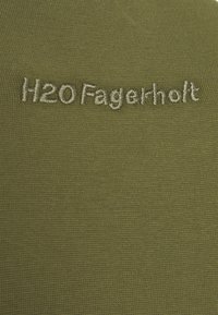 Tejido verde oliva con una trama texturizada; presenta el logo bordado "H2O Fagerholt" en hilo gris claro en la parte superior.