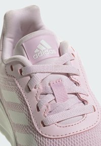 Sneaker Adidas rosa chiaro con tomaia in rete, lacci piatti e linguetta imbottita. Presenta tre strisce bianche sul lato e dettagli con il logo.