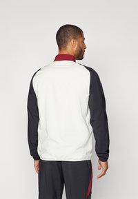 Sportjack met een witte body, zwarte mouwen en een bordeauxrode kraag. Heeft een gladde textuur en een ontspannen pasvorm.