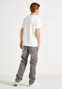 T-shirt en coton blanc à manches courtes, associé à un jean denim gris ample. La tenue est complétée par des baskets blanches sans marque visible.