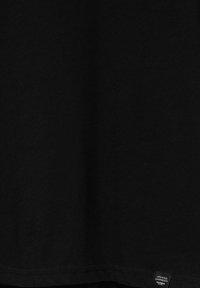 Tessuto nero con un piccolo etichetta rettangolare vicino all'orlo che mostra il testo "Updated Garments Pull&Bear".