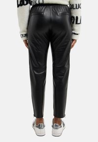 Schwarze Kunstlederhosen mit einer taillierten Passform, ausgestattet mit einem hohen Bund, Gesäßtaschen und Reißverschlüssen an den Knöcheln.