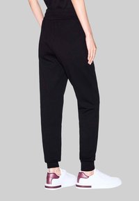 Zwarte joggingbroek met een elastische tailleband, taps toelopende pijpen en zijzakken, gecombineerd met witte sneakers met een bordeauxrode accenten.