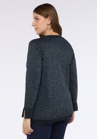 Maglione textured blu scuro con maniche lunghe, fessure laterali e un orlo a coste in contrasto. Il tessuto presenta un motivo maculato su tutta la superficie.