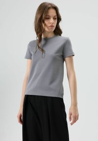 Grijs T-shirt met korte mouwen van zachte stof, met een ronde hals en een losse pasvorm. Gecombineerd met zwarte, loszittende broek.