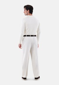 Wei�ßer gerippter Pullover mit langen Ärmeln, kombiniert mit cremefarbenen, hoch taillierten, weiten Hosen und einem schwarzen Gürtel. Legere Schuhe runden das Outfit ab.