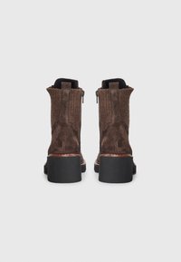 Botas de tornozelo em camurça castanha com um painel de malha texturizada, interior forrado e saltos robustos em borracha preta. Zíperes laterais para fácil calçar.