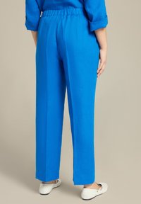 Pantaloni in lino blu con una vestibilità rilassata, vita elasticizzata, gambe dritte e lunghezza cropped, abbinati a scarpe bianche senza lacci.