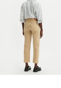 Jeans beige de cintura alta con pierna entallada, bolsillos traseros con costura clásica, combinados con una camisa de manga larga a rayas.