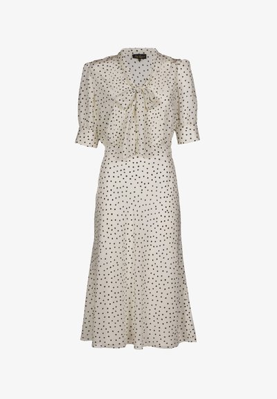 Bézs ruha fekete pöttyökkel, rövid pufó ujjakkal, nyakkendős megoldással és légies szoknyával. Sima anyagból készült, derekánál testhezálló.