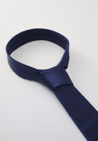 Navy satin kauluskirja, jossa on sileä rakenne, kapea muotoilu ja solmittu viimeistely, aseteltuna yksinkertaiselle valkoiselle taustalle.