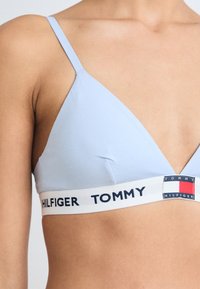 Lyseblå trekantet bralette med tynne stropper og kontrasterende hvit kant med "TOMMY HILFIGER"-logo i marineblå. Myk jerseytekstur.