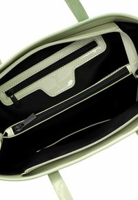 Interno della borsa tote verde in pelle verniciata con fodera nera, una tasca con zip e numerosi scomparti per l'organizzazione.