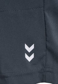 Marinblått tyg med en slät yta och en vit chevronlogotyp tryckt. Sömmar synliga längs kanten, strukturerad och minimalistisk design.