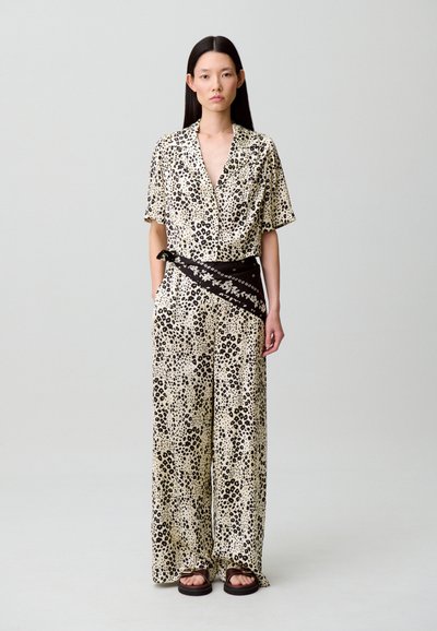 Mono estampado de leopardo en crema y negro, de mangas cortas, piernas anchas, ceñido a la cintura con un cinturón con detalle floral negro, combinado con sandalias marrones.