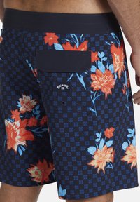 Costume da bagno floreale blu navy con fiori rossi e blu, motivo a quadri, tasca posteriore con pattina e logo sul lato sinistro.