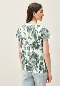 Camiseta de manga corta en verde claro con un patrón de hojas. Está hecha de una tela suave, tiene un cuello redondo y un corte relajado.