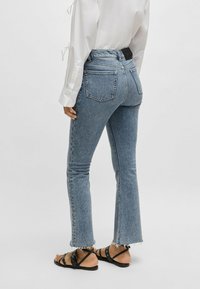 Ljusblå denimjeans med utsvängd byxben och fransade fållar, med en midjehöjd av medelhöjd och bakfickor, kombinerade med svarta sandaler med remmar.