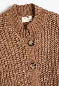 Brązowy sweter kardigan z dzianiny o prążkowanej fakturze, z wysokim kołnierzem i dużym, okrągłym brązowym guzikiem do zapięcia.