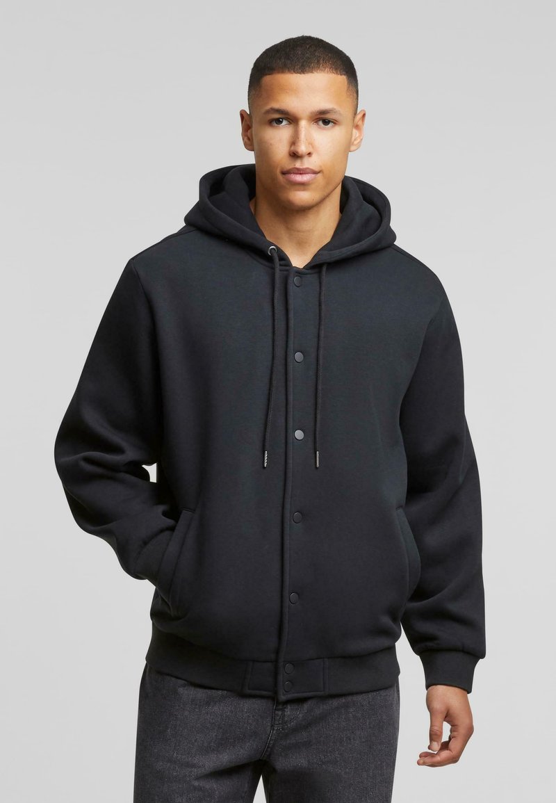 Zwarte hoodie met voor knopen, trekkoorden en zijzakken. Zachte textuur, relaxte pasvorm en ribgebreide manchetten en tailleband.