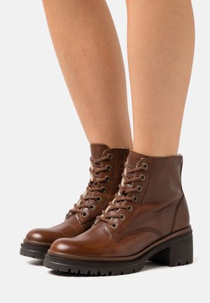 Brązowe skórzane botki za kostkę z okrągłym noskiem, sznurowanym przodem, wyściełanym kołnierzem i grubym obcasem. Teksturowana powierzchnia z kontrastującymi detalami w szwach.
