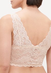 Lace bralette in nude with floral patterns, wide scalloped straps, and a V-back design, featuring a soft, textured finish.