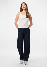 Canotta bianca a costine con un piccolo dettaglio a fiocco, abbinata a jeans in denim scuro a vita alta e gamba larga, e sneakers grigie.