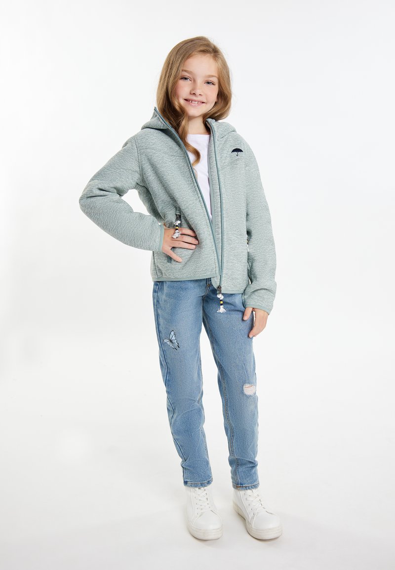 Ljusgrå zip-up hoodie i texturerat tyg, med en framstående logotyp och snörning. Matchad med blå slitna jeans och vita sneakers.