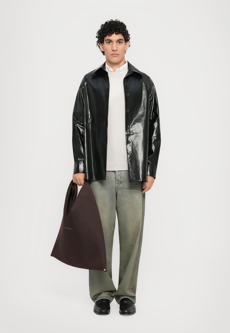 Black shiny leather button-up shirt, light gray knit sweater, gray-green wide-leg pants, holding maroon fabric tote bag, black shoes.