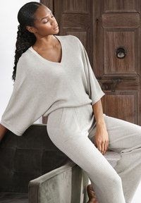 Lichtgrijze geribbelde breiselset met een oversized V-hals top en taps toelopende broek met zakken, gekenmerkt door een gezellige textuur.