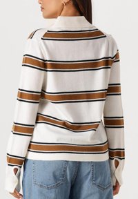 Stripet genser i krem, brun og svart. Har krage og utskjæring ved mansjettene. Myk, teksturert strikket stoff.