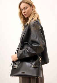 Melnas ādas rokas soma ar zelta metāla akcentiem, strukturēta dizaina un dubultiem rokturiem. Gluda tekstūra ar sprādžu detaļām sānos.