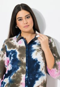 Camisa de botones con un patrón de tie-dye en marrón, azul y rosa. La tela tiene un aspecto texturizado, con cuello y parte delantera de botones.